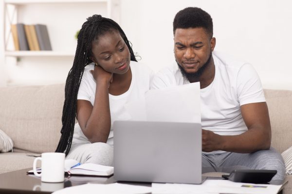 Black couple managing family budget at home together, reading financial documents