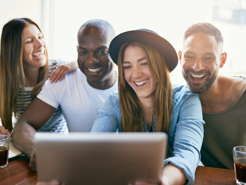 Cheerful group of young co-workers sharing tablet