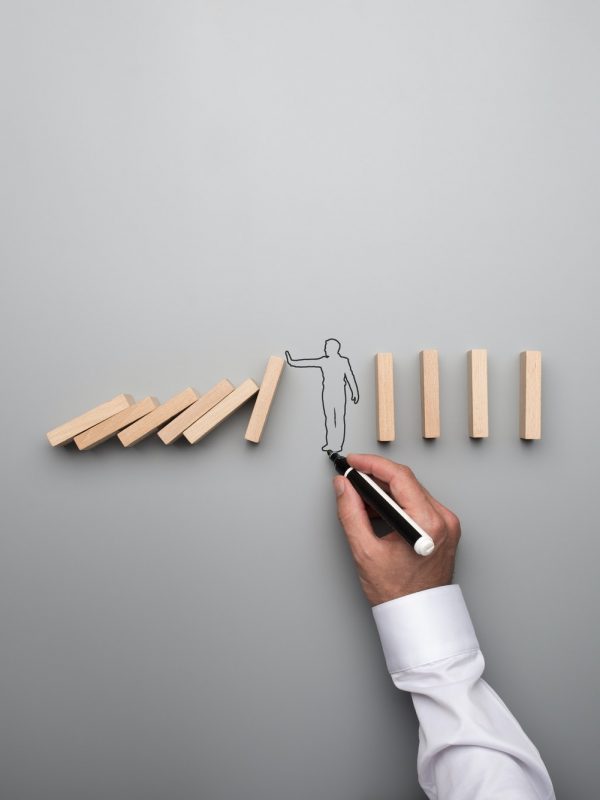 Man drawing the outline of a businessman stopping the domino eff