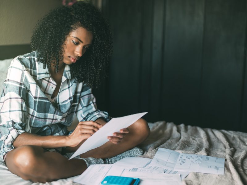 worried black woman with bills and finance problems on bed
